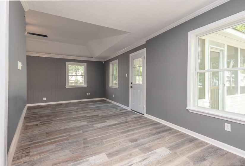 Spacious room featuring wood-finish flooring, neutral gray walls, white trim, and multiple windows