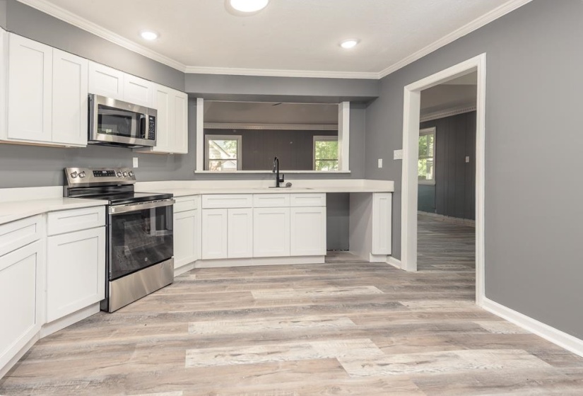 Kitchen featuring wood-finish flooring, white cabinetry, integrated stainless steel appliances, light-toned countertops, and a pass-through window