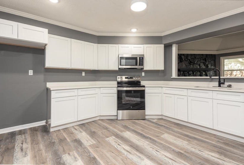 Contemporary kitchen featuring white cabinetry, light-toned countertops, stainless steel appliances, and wood-finish flooring
