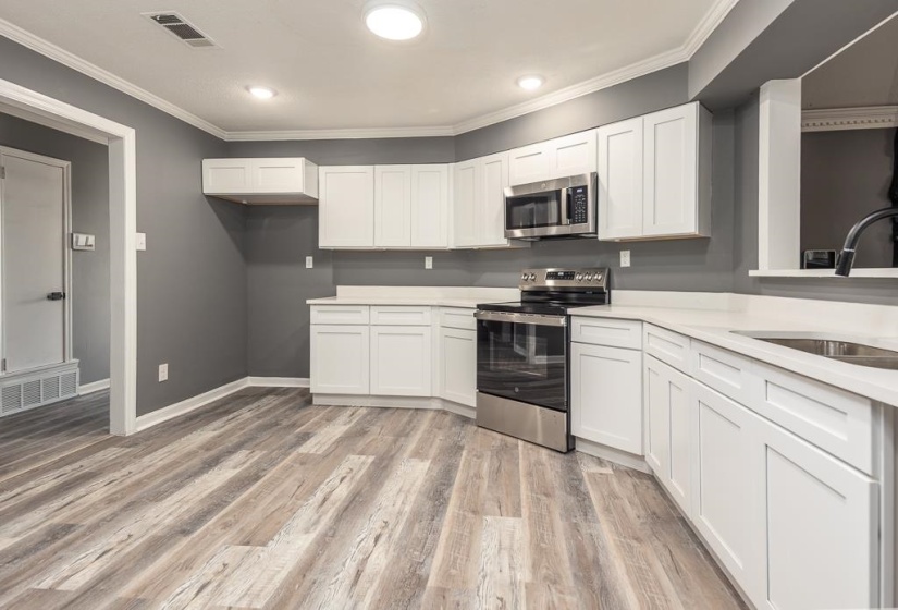 Kitchen featuring wood-finish flooring, white cabinetry, integrated stainless steel appliances, light-toned countertops, and recessed lighting