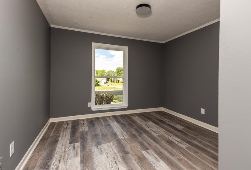 Room featuring wood-finish flooring, a single window with white trim, and a flush-mount ceiling light fixture