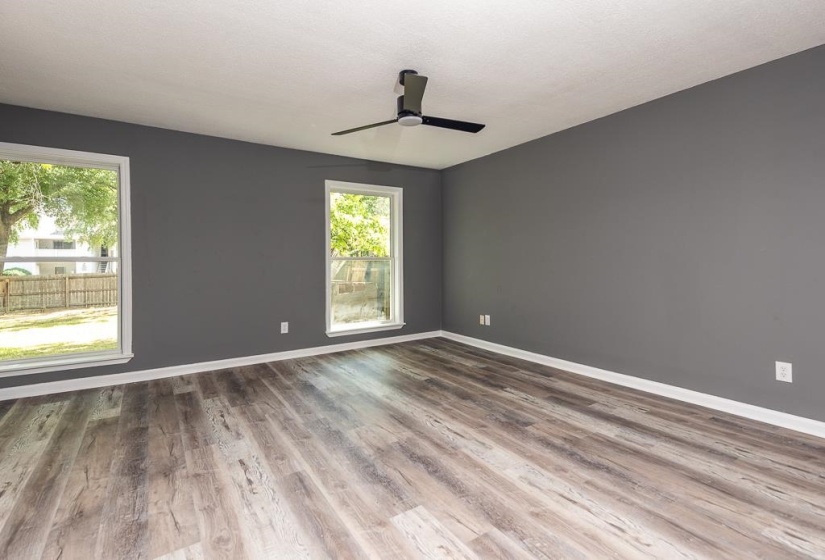 Spacious room featuring wood-finish flooring, two large windows with white trim, a modern black ceiling fan, and grey painted walls with white baseboards