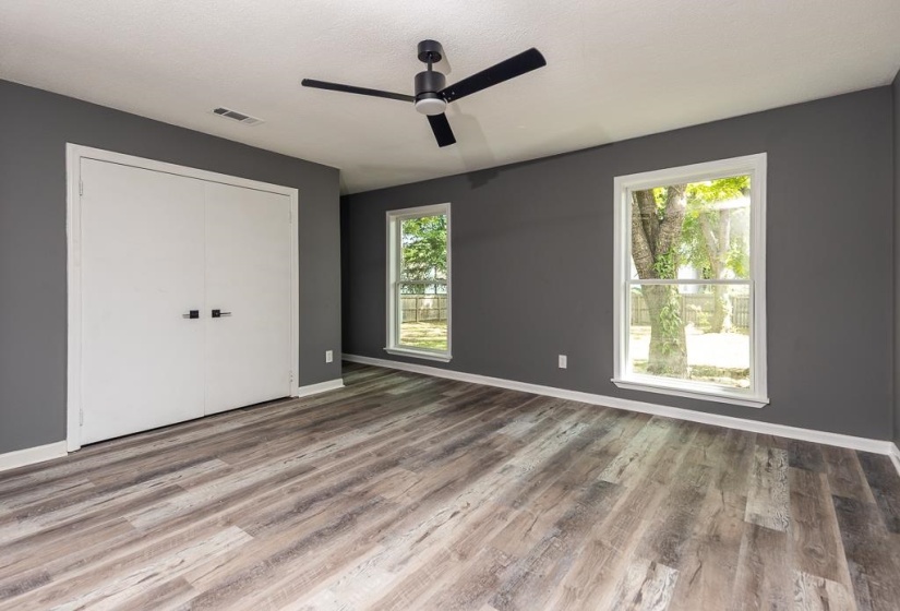 Spacious room featuring wood-finish flooring, two windows, two-door closet, ceiling fan, and dark gray wall color