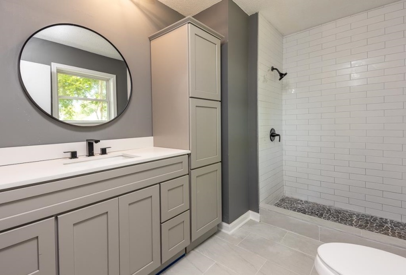 Bathroom featuring a light gray vanity with white countertop, black fixtures, and a circular mirror