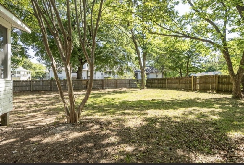 Expansive backyard featuring a partial wooden privacy fence, mature trees, and a screened porch visible on the side of the dwelling