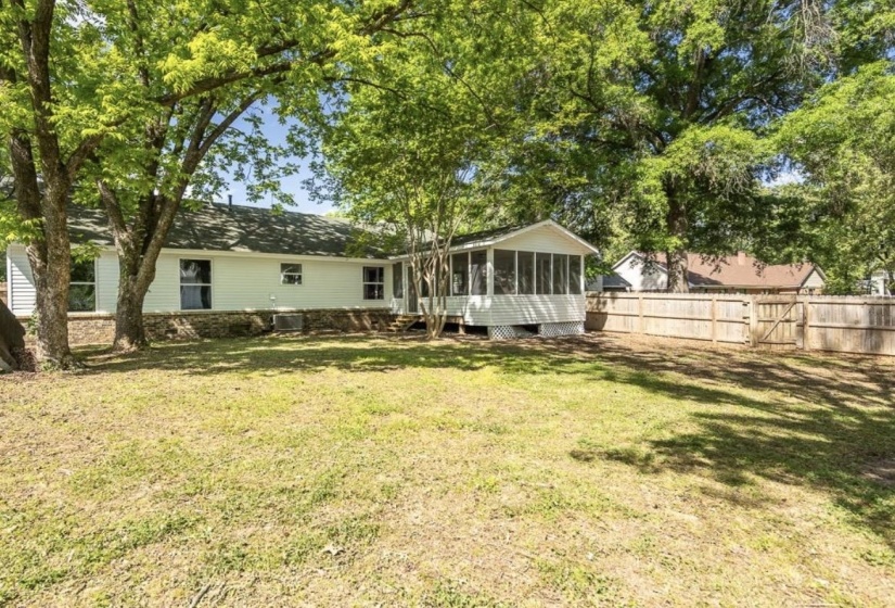 Spacious backyard featuring a screened porch, privacy fence, mature trees, and a white siding exterior with a stone foundation