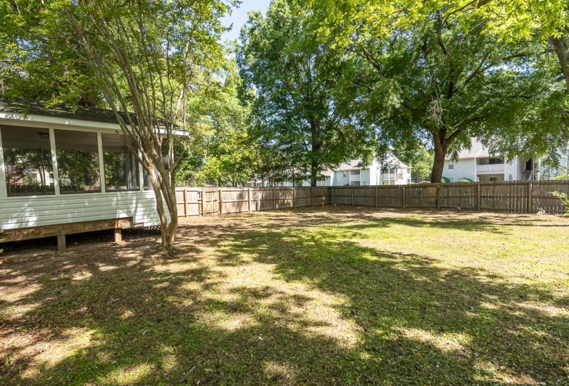 Expansive backyard featuring a screened porch with white siding, mature trees, a manicured lawn, and a perimeter wood fence
