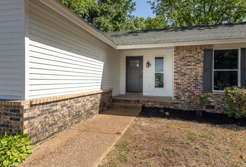 Exterior featuring a dark gray paneled entry door, white siding, and a partial brick facade