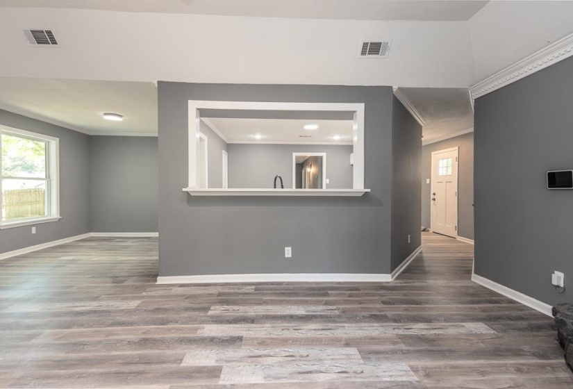 Spacious room featuring wood-finish flooring, neutral gray walls, white trim, and a pass-through opening