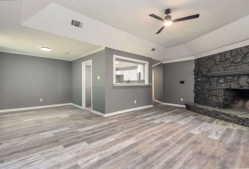 Spacious living area featuring wood-finish flooring, a prominent stone fireplace, and a ceiling fan