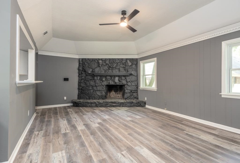 Spacious living area featuring a prominent stone fireplace, vaulted ceiling with a ceiling fan, and wood-finish flooring