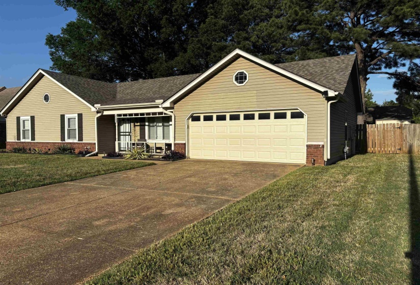 Ranch-style residence featuring light-toned siding with dark shutters, an attached two-car garage, and a covered porch entry