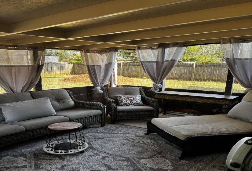 Screened-in porch featuring a wood-beam ceiling, privacy curtains, and a view of the fenced backyard