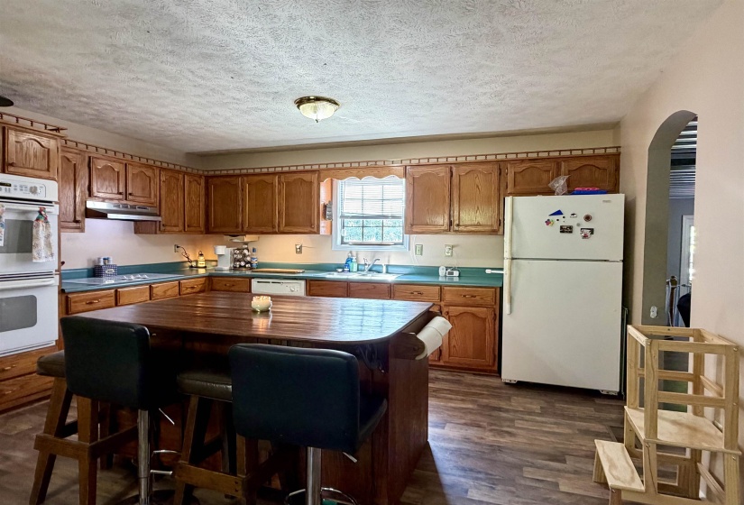 Kitchen featuring wood-finish flooring, a central island with seating, wood cabinetry, a double oven, and a built-in dishwasher