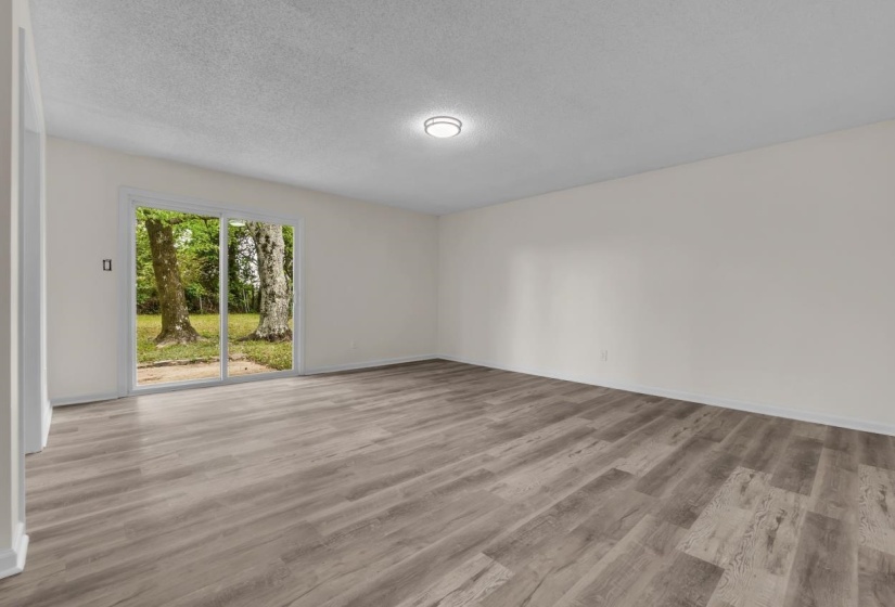 Spacious room featuring wood-finish flooring, white walls, and a sliding glass door providing access to the exterior