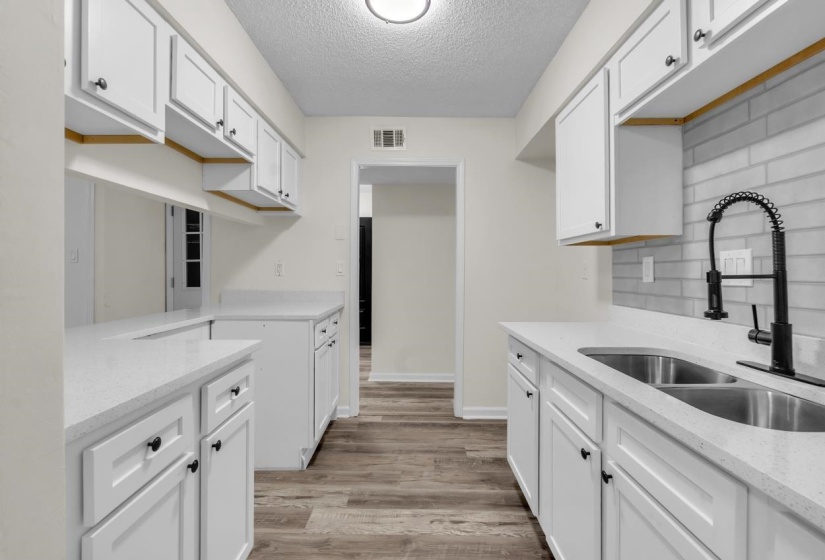 Modern kitchen featuring white shaker cabinetry, light-colored countertops, a double basin stainless steel sink with a black pull-down faucet, a subway tile backsplash, and wood-finish flooring