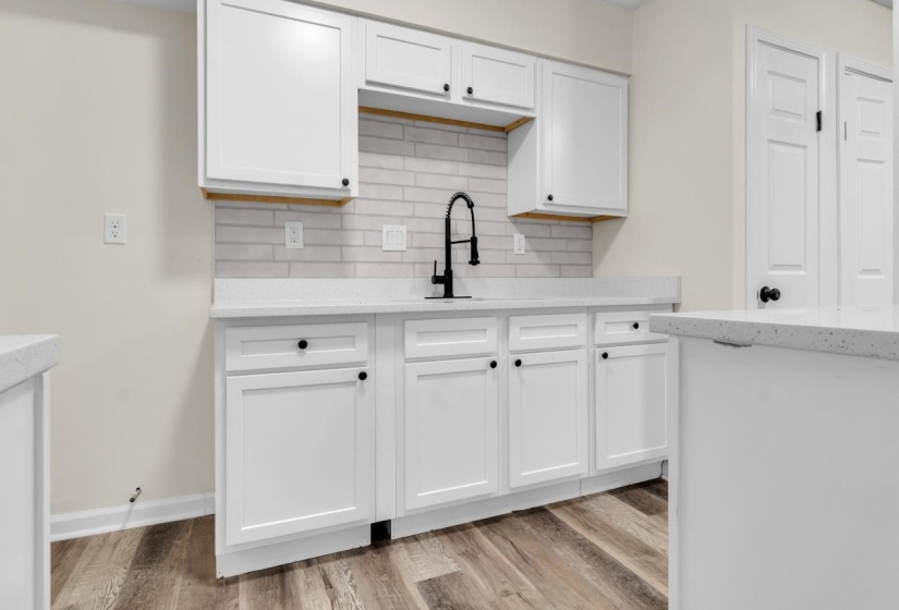 Modern kitchen featuring white shaker cabinetry, light-toned countertops, a subway tile backsplash, and wood-finish flooring