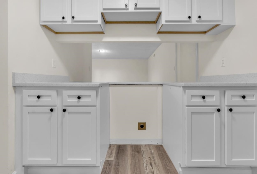 White shaker-style cabinetry with black hardware, light-toned countertops, and wood-finish flooring