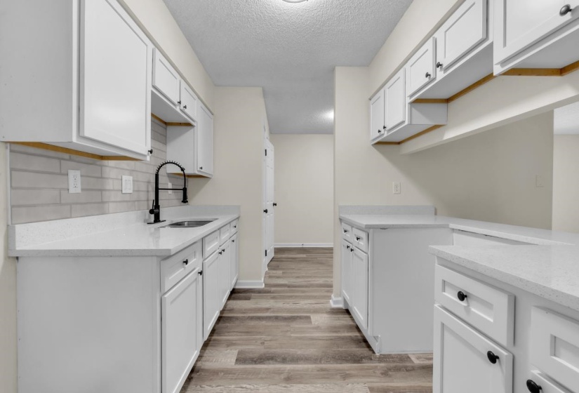 Bright kitchen featuring white cabinetry, light-toned countertops, a stainless steel sink with a matte black faucet, a light subway tile backsplash, and wood-finish flooring