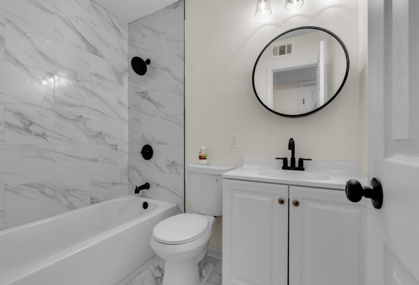 Full bathroom featuring a white tub, shower with marble-look tile surround, toilet, and vanity with a white countertop
