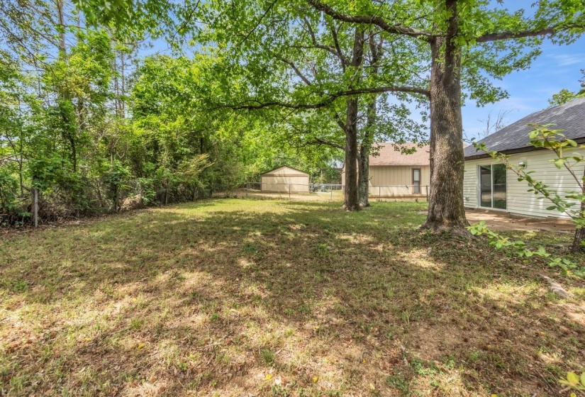 Spacious backyard featuring established trees, a grassy lawn, and a back patio with sliding glass doors