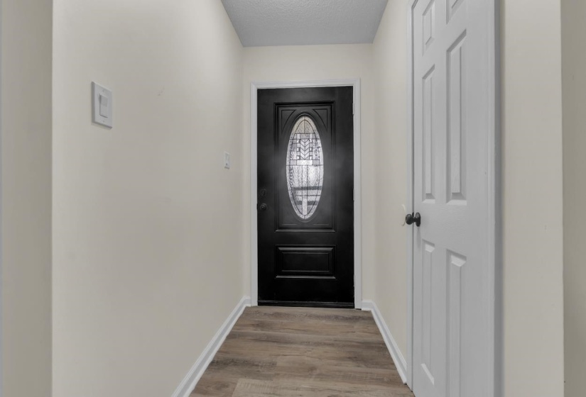 Foyer featuring a dark-finish entry door with an oval decorative glass insert, wood-finish flooring, and light-toned walls