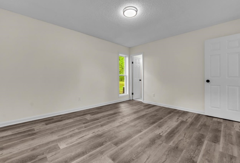 Spacious interior room featuring wood-finish flooring, neutral wall tones, and a window providing natural light