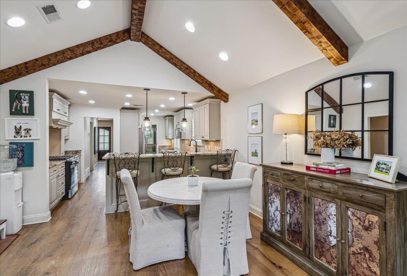 Open-concept living space featuring vaulted ceilings with exposed wood beams, wood-finish flooring, a kitchen with a breakfast bar, and recessed lighting