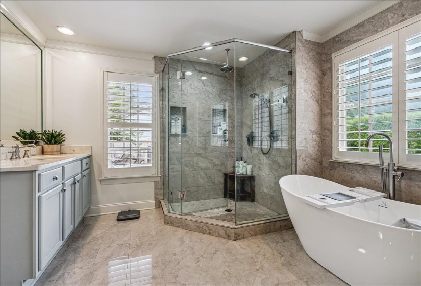 Spacious bathroom featuring a frameless glass shower enclosure, freestanding soaking tub, dual shower heads, and marble-finish tile flooring