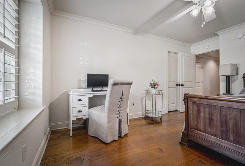 Hardwood flooring throughout featuring a window with plantation shutters, a ceiling fan with integrated lighting, and crown molding
