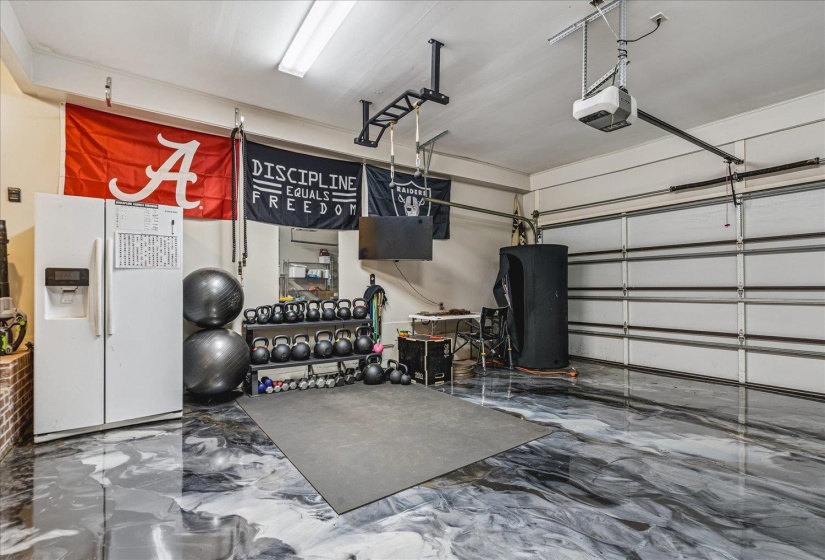 Garage space featuring a patterned epoxy floor, white paneled garage door, ceiling-mounted lighting, and a ceiling-mounted garage door opener