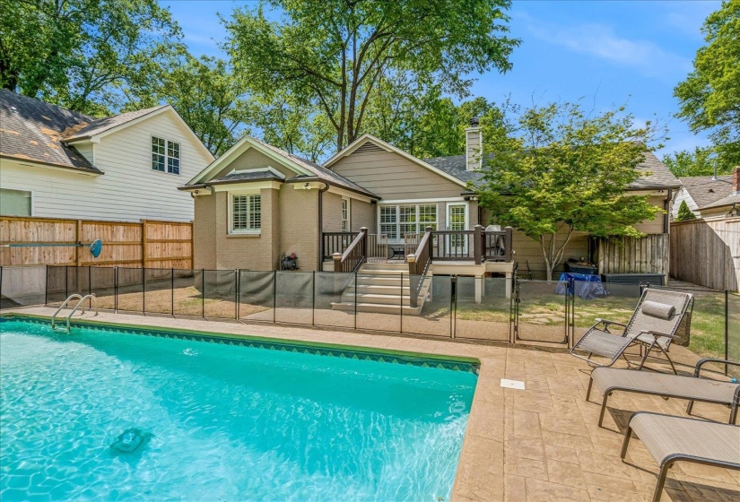 In-ground swimming pool with stamped concrete decking, surrounded by a removable safety fence
