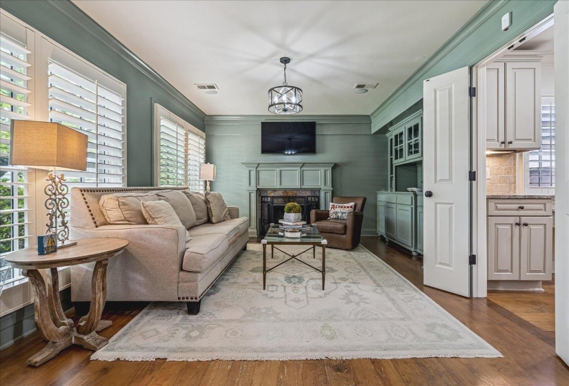 Living area featuring hardwood flooring, plantation shutters, a decorative fireplace with a mantel, and built-in cabinetry