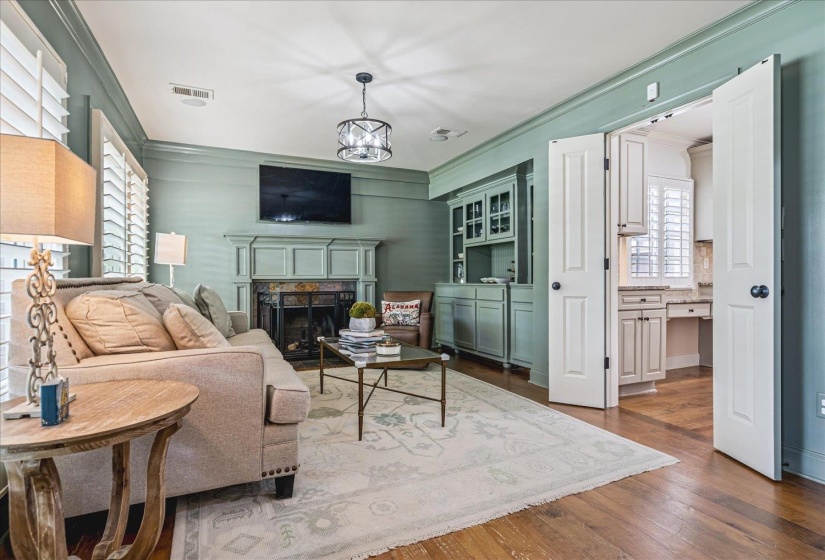 Living area featuring wood-finish flooring, a fireplace with a detailed mantel, and plantation shutters
