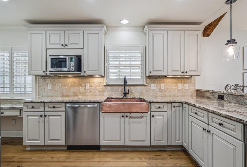 Kitchen featuring light-toned cabinetry, a large copper farmhouse sink, stainless steel appliances, granite countertops, and wood-finish flooring