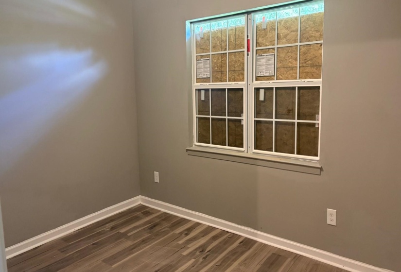 Room featuring wood-finish flooring, neutral wall paint, white baseboards, and a window with white sashes and grilles