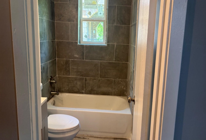 Bathroom featuring a white bathtub, dark gray subway tile surround, and a window with decorative glass