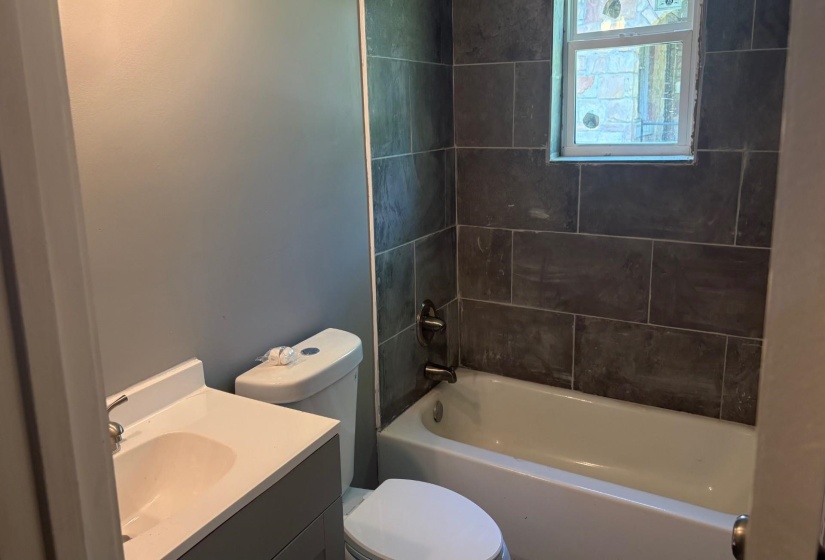 Bathroom featuring a white bathtub, dark gray subway tile surround, and a window with frosted glass