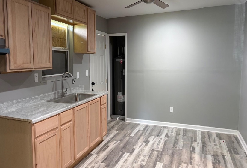 Kitchenette featuring wood-finish cabinetry, stainless steel sink with a gooseneck faucet, light-toned countertop, and wood-look flooring
