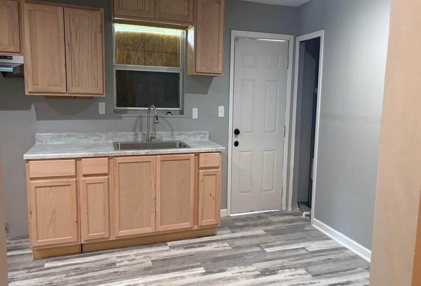 Kitchen area with light wood cabinetry, a stainless steel sink with a high-arc faucet, and light gray countertops