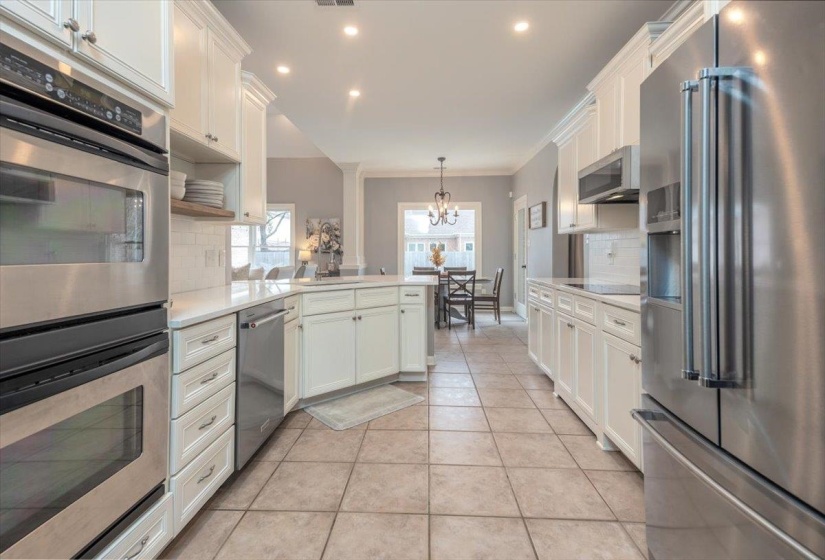 Kitchen featuring extensive white cabinetry, stainless steel appliances, light-toned countertops, subway tile backsplash, and tile flooring