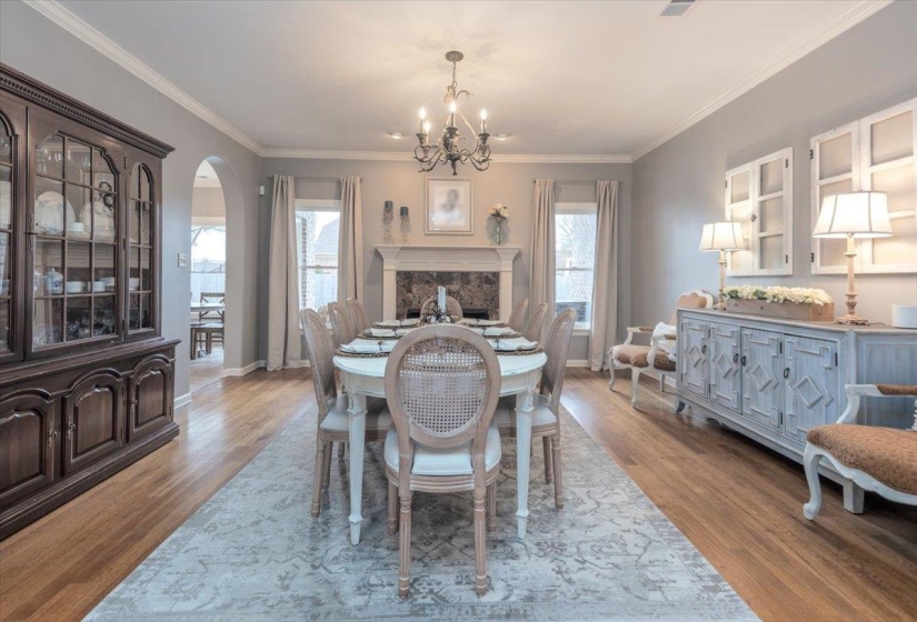 Spacious dining area featuring wood-finish flooring, a decorative fireplace with a stone surround, and an arched entryway