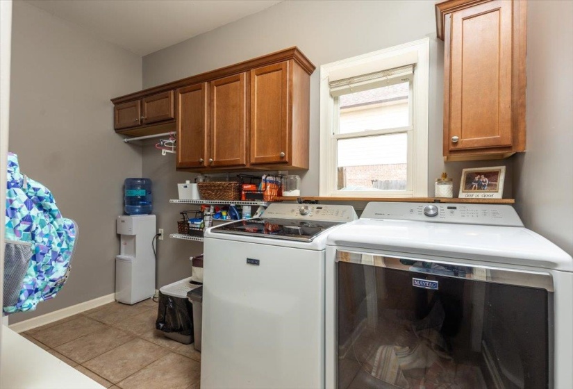 Dedicated laundry room featuring tile flooring, wooden cabinetry, and a window for natural light