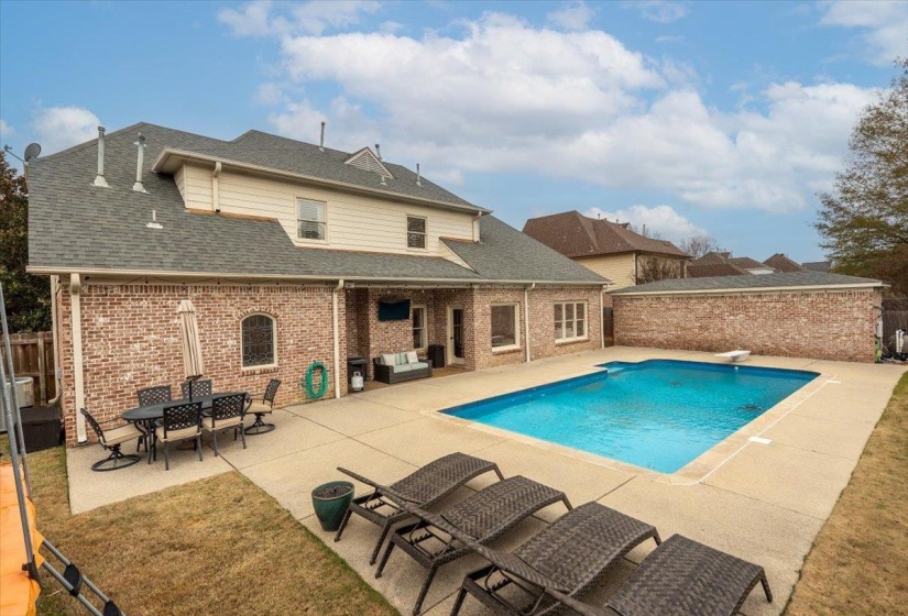 Expansive backyard featuring a rectangular swimming pool, concrete patio, and mature lawn
