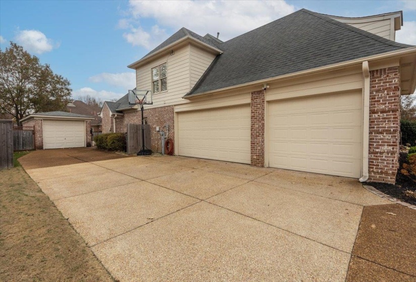 Exterior featuring a two-car garage with cream-colored doors, red brick accents, light siding, and a shingled roof