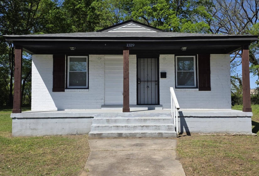 White brick exterior with a front porch, featuring dark wood-finish support columns and a dark gray roof