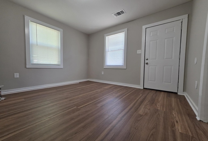 Room featuring wood-finish flooring, two windows with blinds, a white paneled door, and neutral wall paint