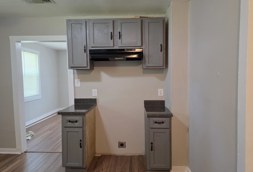 Kitchenette featuring gray shaker-style cabinetry, dark speckled countertops, and a black range hood