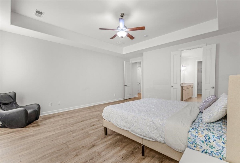 Spacious sleeping area featuring wood-finish flooring and a tray ceiling with a ceiling fan