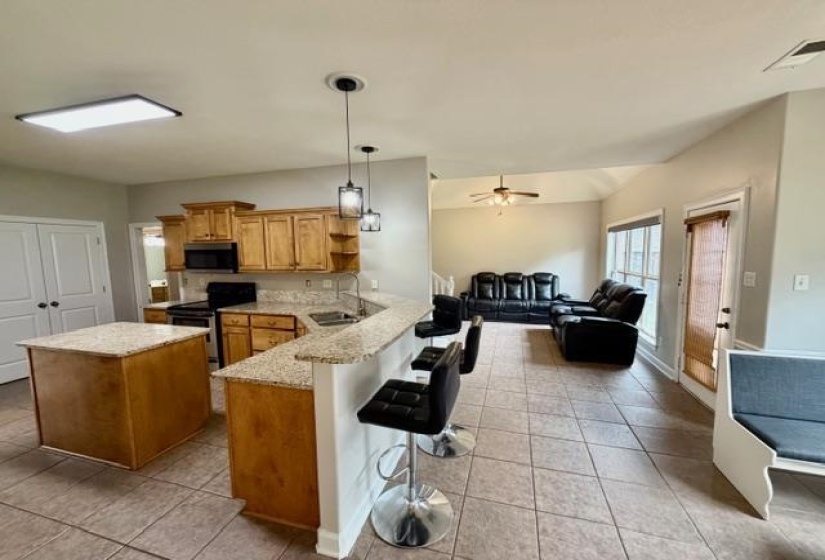 Open-concept kitchen and living area featuring granite countertops, wood cabinetry, a central island, tiled flooring, and pendant lighting